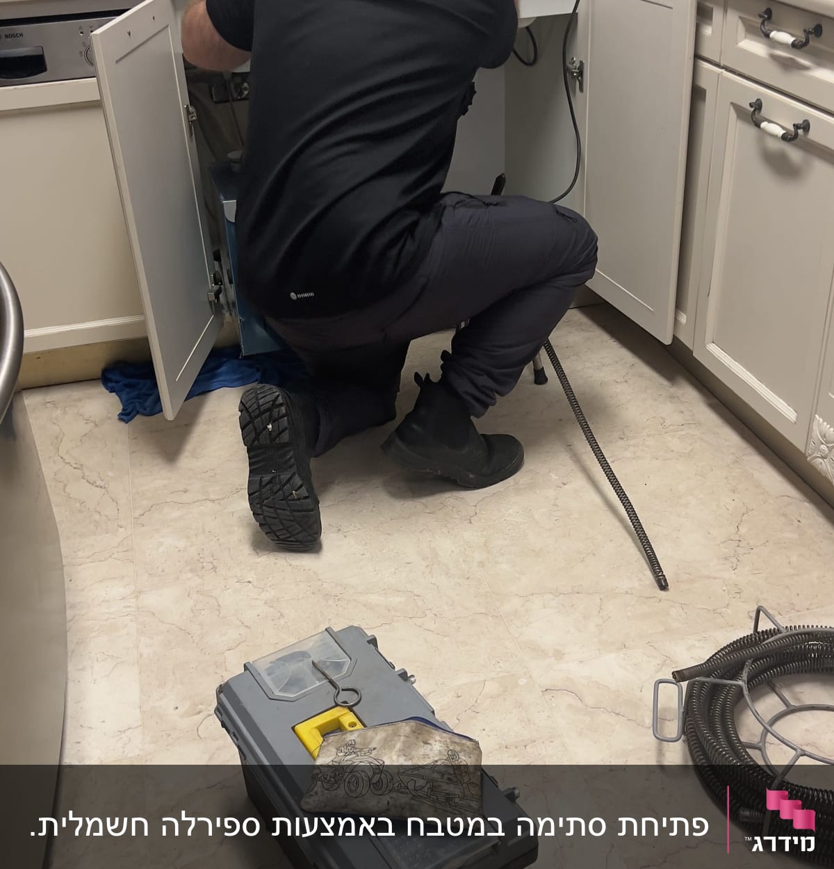 אינסטלטור עובד מתחת לכיור עם כלי עבודה וצינור